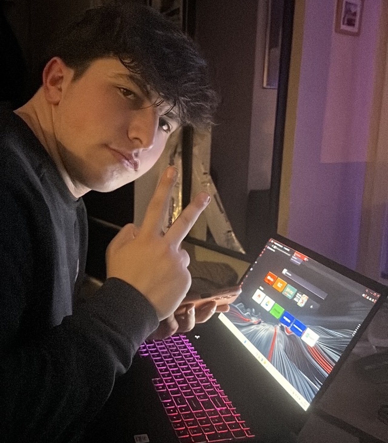 A photograph of a man holding up two fingers beside a laptop